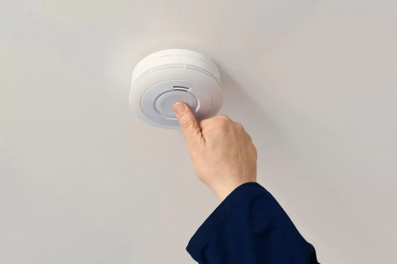 Pressing the button to test a smoke alarm on the ceiling.